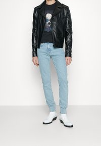 Svart läderbikerjacka, grafisk svart t-shirt, ljusblå skinny jeans och vita ankelstövlar med svarta sulor. Enkelt design och passform.