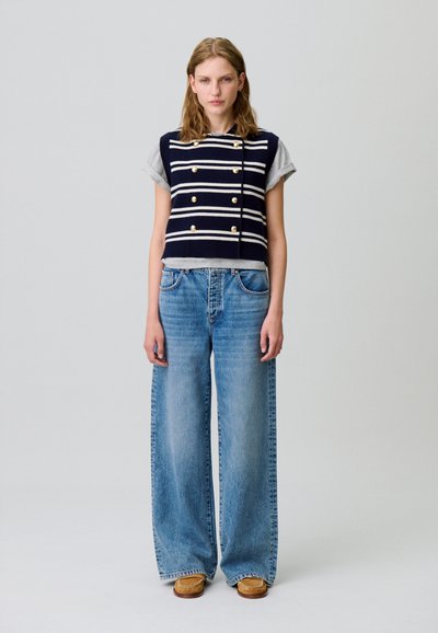 Croc top a righe blu navy e bianche con bottoni dorati, abbinato a jeans a gamba larga celesti e mule in camoscio marroni.