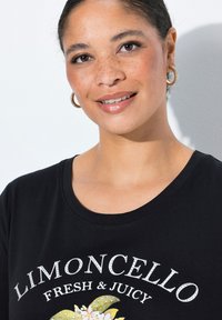 Camiseta de algodón negra con un diseño floral que incluye el texto "Limoncello Fresh & Juicy" en acentos blancos y plateados. Manga corta, escote redondo.