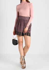 Rosa långärmad polotröja kombinerad med en mönstrad kjol i färger som lila och grön, med svarta och vita randiga detaljer. Metalliska ankelskor och en liten svart handväska fulländar outfiten.