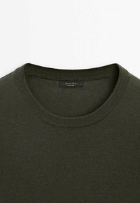 Pull col rond vert foncé avec col côtelé et une petite étiquette noire cousue à l'intérieur de l'arrière du col.