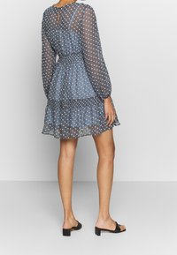 Blå mönstrad klänning med genomskinliga långa ärmar, elastisk midja och volangnedd. Tillsammans med svarta sandaler utan häl, som visar en minimalistisk design.