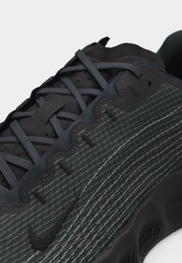 Κοντινή λήψη μαύρου αθλητικού παπουτσιού Nike με υφή στην πλαϊνή επιφάνεια, ορατά κορδόνια και κεντημένο λογότυπο Nike swoosh.