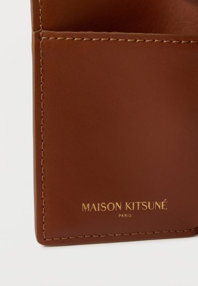 Καφέ δερμάτινο πορτοφόλι με κομψό σχεδιασμό, που διαθέτει χρυσό ανάγλυφο λογότυπο "MAISON KITSUNÉ PARIS" και διακριτικές λεπτομέρειες ραφής.
