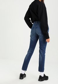 Jeans de mezclilla azul de cintura alta con pierna ajustada. Presentan un diseño de bolsillo trasero y un ligero desvanecimiento, combinados con zapatillas deportivas negras.