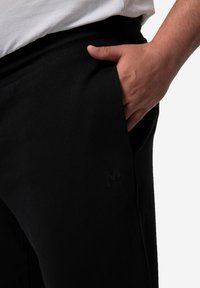 Zwarte trainingsbroek van een katoenmix, met een geribde tailleband, zijzak en subtiele logo-accent op het onderbeen.