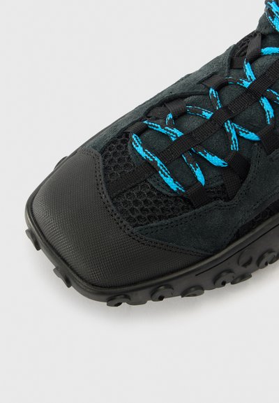Black athletic shoe with a mesh and suede upper, featuring blue laces and a textured rubber outsole with circular patterns.