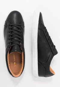 Baskets en cuir noir à texture lisse, semelle en caoutchouc blanche et design minimaliste. Dotées de lacets noirs et d'une doublure intérieure couleur sable.