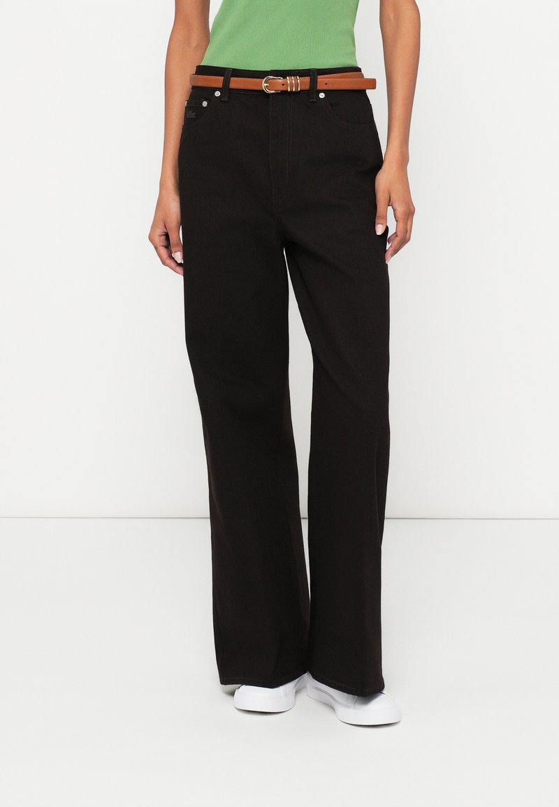 Μαύρο τζιν με φαρδιά πόδια κατασκευασμένο από ανθεκτικό ύφασμα, με καφέ δερμάτινη ζώνη, ασημένια μεταλλικά στοιχεία και μπροστινές τσέπες. Ομαλή υφή και καθαρό σχέδιο.