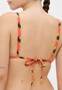 Kleurige bikini-top met dunne banden in rood, geel en zwart, met een striksluiting op de rug en verstelbare hardware.