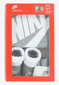 Set pentru bebeluși Nike, compus din trei piese: un body gri, șosete gri și albe și o căciulă, toate prezentate într-o cutie roșie cu fereastră transparentă.