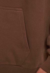 Felpa marrone con tasca a marsupio, polsini e orlo a coste. Il materiale ha una texture liscia con dettagli di cucitura visibili.