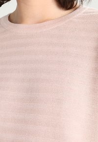 Helle rosa Strickpullover mit geripptem Muster und rundem Ausschnitt. Der Stoff zeigt dezente horizontale Streifen. Weiches und atmungsaktives Material.