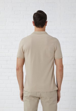 Beige poloshirt met korte mouwen en een kraag, met een gladde textuur en subtiele stiksel details, gecombineerd met lichtbeige broek.