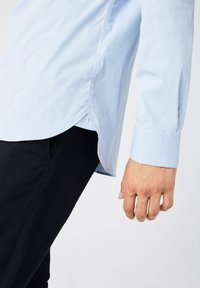 Camicia a righe blu chiaro con orlo curvo e polsini abbottonati, abbinata a pantaloni neri a gamba affusolata. Tessuto morbido e leggero.