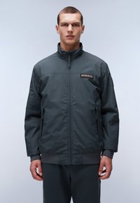 Giubbotto bomber da uomo grigio scuro con colletto rialzato, chiusura con zip, due tasche laterali, polsini a costine e una patch logo sul petto.