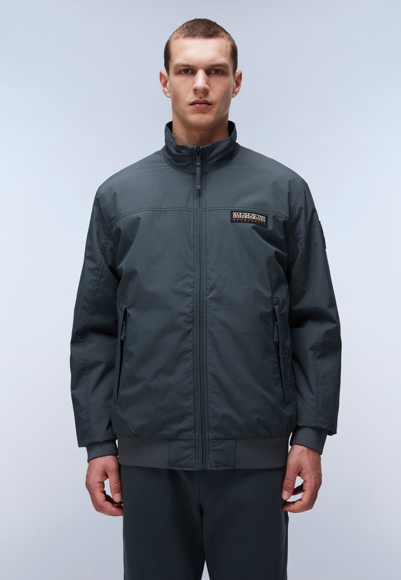 Giubbotto bomber da uomo grigio scuro con colletto rialzato, chiusura con zip, due tasche laterali, polsini a costine e una patch logo sul petto.