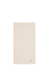 Lys beige vævet tæppe med en blød tekstur, rektangulær form og et lille logo i nederste højre hjørne.