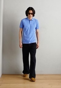 Polo de culoare albastru deschis, pantaloni negri, pantofi maro și ochelari de soare. Cămașa are guler, iar pantalonii sunt drepți.