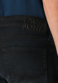 Sorte denim jeans har en tekstureret talje med et hævet logo. Designet inkluderer en baglomme med subtile sydetaljer.