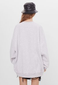 Överdimensionerad grå sweatshirt med nedhängda axlar och ribbad nederkant. Kombinerad med en svart bucket hat och fransiga denimshorts. Enfärgad tygtextur.