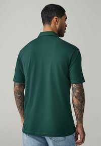 Grüne Poloshirt mit kurzen Ärmeln, hergestellt aus einem glatten Stoff. Verfügt über einen klassischen Kragen und eine dezente Textur. Rückansicht angezeigt.