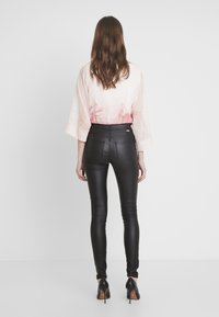 Top de gran tamaño en rosa claro con una textura suave y un diseño en degradado, combinado con pantalones de cuero sintético negro de cintura alta con bolsillos traseros.