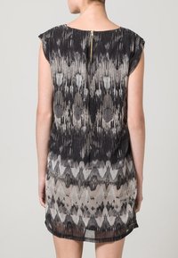 Vestido de manga corta con un patrón abstracto en negro y gris, hecho de una tela ligera con cierre de cremallera en la parte posterior. Dobladillo semitransparente.
