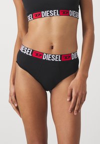 Sorte bomullsunderbukser med en kontrasterende rød og hvit DIESEL-logo på midjebåndet. Har en glatt tekstur og en klassisk brief-snitt.
