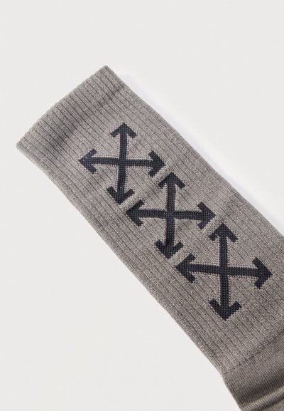 Chaussette grise côtelée avec trois symboles de flèches noires multidirectionnelles tricotés en ligne verticale sur le tissu.