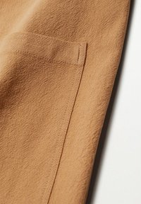 Kangasta, jossa on teksturoitu pinta, etutasku ja yksityiskohtainen ompelu. Materiaali näyttää pehmeältä ja hieman ryppyiseltä.