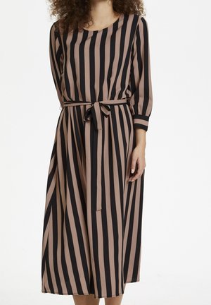 Frau trägt ein braun-schwarz gestreiftes Midikleid mit drei Viertel Ärmeln und einem gebundenen Taillengürtel.