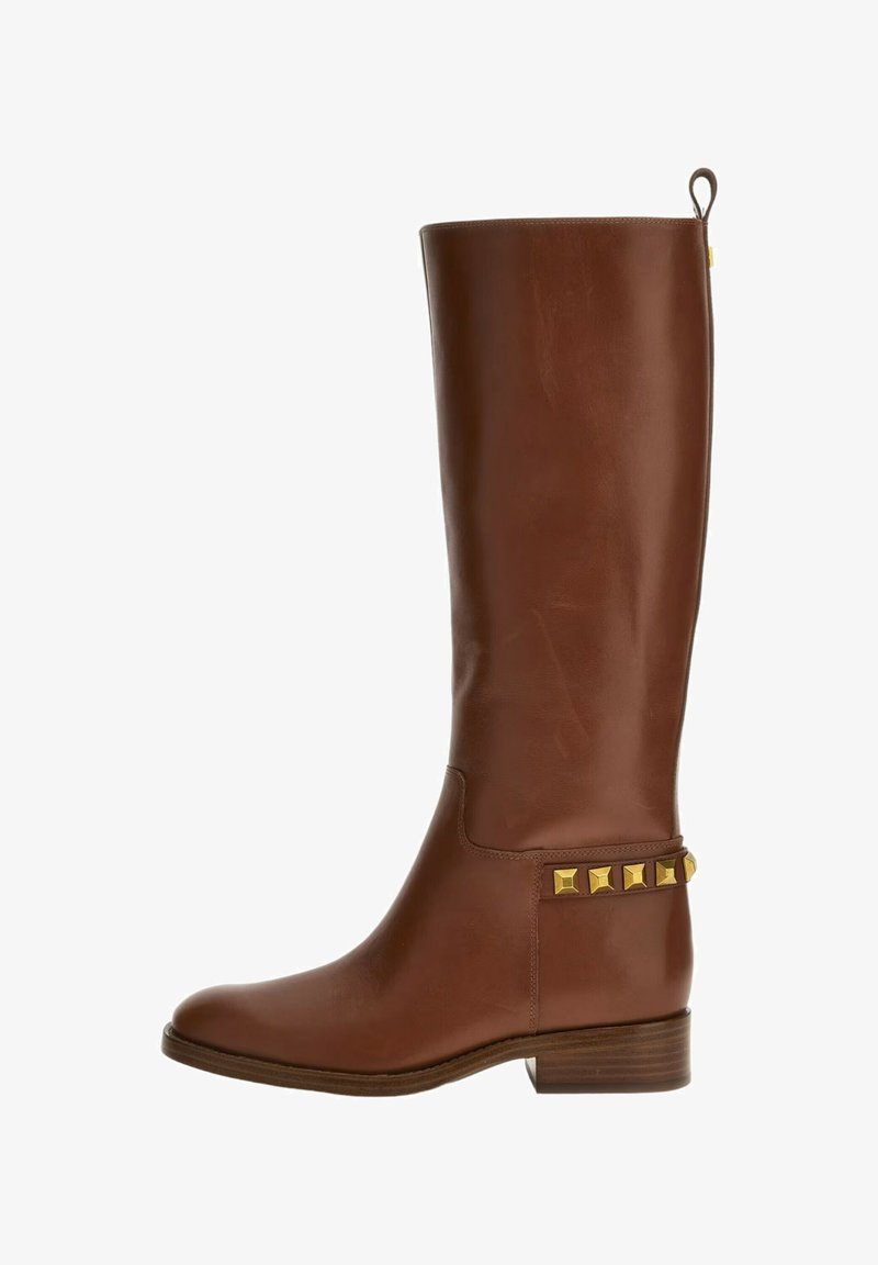 Bruine leren kniehoge laars met een gladde afwerking, lage gestapelde hak en gouden studs langs de enkel voor extra detail.