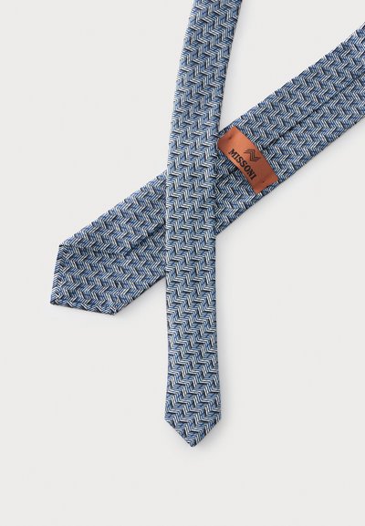 Cravate à motif chevron bleu et blanc avec une étiquette marron indiquant la marque Missoni, posée à plat sur fond blanc.