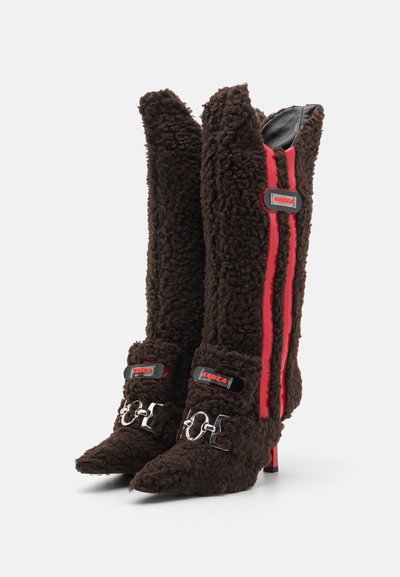 Botas de tacón alto marrones con textura, rayas laterales rojas, acentos metálicos y hebillas. Material suave con un diseño de punta afilada.