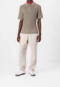 Beige stickad polo-tröja med ett texturiserat mönster, korta ärmar och knäppning med tre knappar. Kombinerad med ljusbeiga linbyxor och vita sneakers.