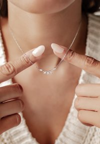 Collier en chaîne argentée mettant en valeur cinq accents ressemblant à des gemmes, avec un design délicat et une finition polie, tenu entre des doigts sur un fond clair.