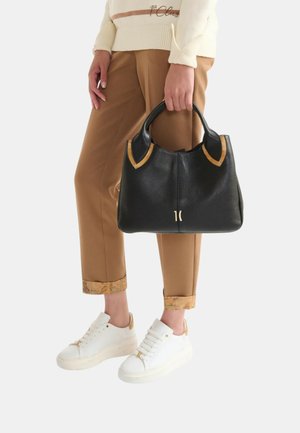 Borsa in pelle nera con dettagli color cuoio, forma arrotondata e hardware dorato. Indossata con pantaloni color cuoio e sneakers bianche con dettagli dorati.