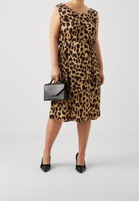 Vestido de estampado de leopardo en tonos de marrón y dorado, con escote en forma de V, cintura ajustada, acompañado de un pequeño bolso negro de textura de cocodrilo.