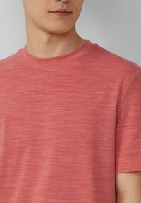 Koraalrode katoenen t-shirt met een ronde hals, korte mouwen en een subtiel textuurpatroon. Stof vertoont een lichte kleurvariatie.