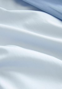 Material textil din bumbac în nuanțe de albastru deschis și alb moale, evidențiind o textură netedă și o strălucire subtilă, cu pliuri și cute delicate.