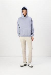 Sweat-shirt à capuche gris clair avec une poche avant, associé à un pantalon crème et des baskets noir et blanc. Coupe simple et décontractée.