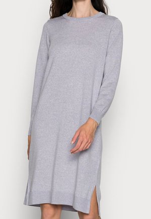 Lichtgrijze gebreide jurk met lange mouwen en zijsplitten, gedragen door een persoon, zichtbaar van halverwege de nek tot de knieën tegen een effen achtergrond.