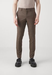 Pantaloni carouri maro cu o croială slim fit, având o textură fină, închidere cu nasture în față și buzunare laterale, asortați cu pantofi cu platformă negri.