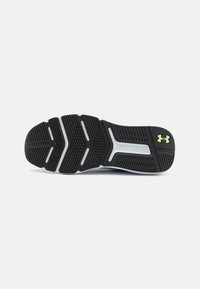 Schwarze Gummisohle mit weißen und grauen Laufmustern sowie einem kleinen grünen Under Armour-Logo in der Nähe der Ferse auf einem weißen Hintergrund.