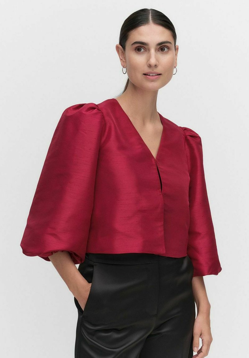 Bordeaux cropped bluse med puffede ærmer, dyb V-hals, glat satin tekstur og frontlukning, parret med sorte bukser.