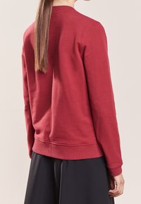 Sudadera roja con cuello y puños de canalé, que presenta una textura de algodón suave y un corte relajado; vista desde la parte posterior.