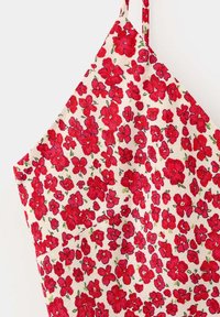 Bande de tissu blanc avec imprimé floral rouge dense avec de petites feuilles vertes, montrée en gros plan sur fond uni.