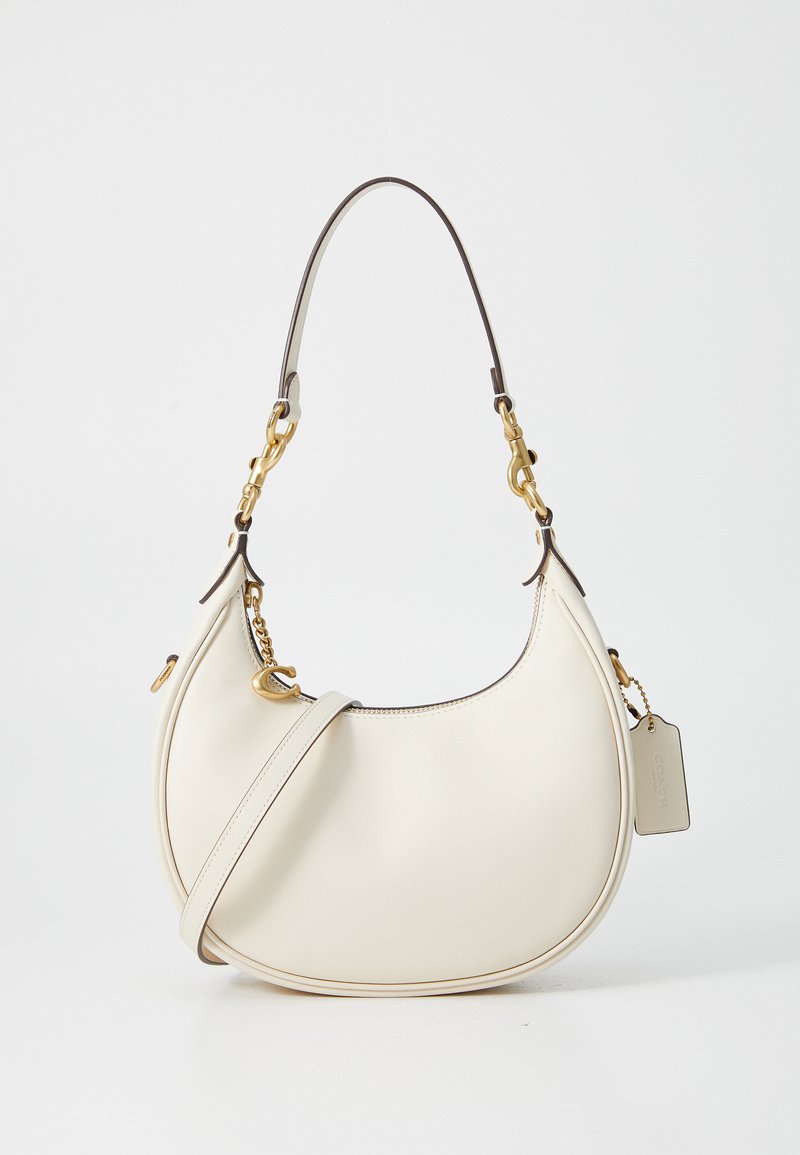 Bolsa de mão de couro creme com uma forma curva, apresentando um detalhe em metal dourado e uma alça ajustável. Textura suave com costura contrastante.