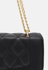 Sac à main en cuir noir avec une bandoulière chaîne dorée, arborant un design matelassé et une texture lisse, mettant en valeur les coutures et les détails métalliques.